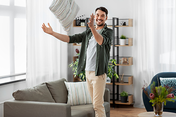 Image showing happy smiling man arranging sofa cushions at home