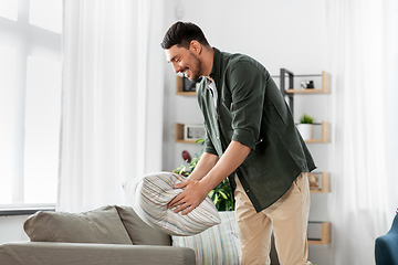 Image showing happy smiling man arranging sofa cushions at home