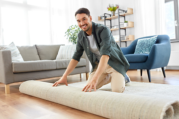 Image showing happy smiling young man unfolding carpet at home