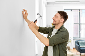 Image showing smiling man hammering nail to wall at home