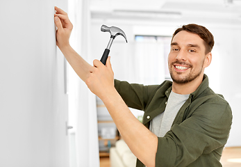 Image showing smiling man hammering nail to wall at home