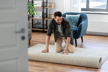 Image showing happy smiling young man unfolding carpet at home