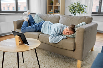 Image showing bored man with tablet pc lying on sofa at home