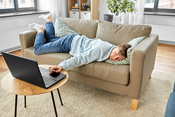 Image showing bored man with laptop lying on sofa at home