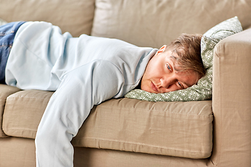 Image showing bored or lazy young man lying on sofa at home