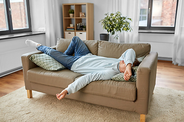 Image showing bored or lazy young man lying on sofa at home