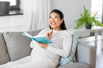 Image showing happy pregnant woman writing to diary at home