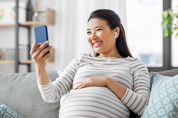 Image showing pregnant woman with phone and earphones at home