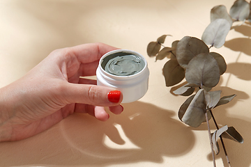 Image showing hand holding jar of blue cosmetic clay mask