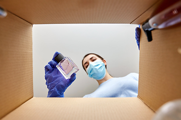 Image showing woman in mask unpacking parcel box with cosmetics