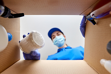 Image showing woman in mask unpacking parcel box with cosmetics