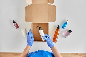 Image showing hands in gloves packing parcel box with cosmetics