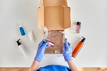 Image showing hands in gloves packing parcel box with cosmetics