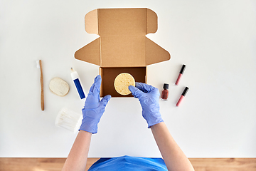 Image showing hands in gloves packing parcel box with cosmetics