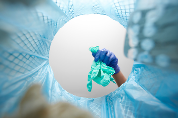 Image showing hand throwing used medical gloves into trash can