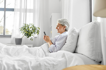 Image showing happy senior woman using smartphone in bed at home