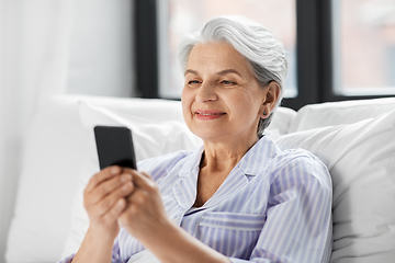 Image showing happy senior woman using smartphone in bed at home