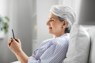 Image showing happy senior woman using smartphone in bed at home