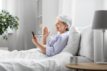 Image showing senior woman with phone having video call in bed