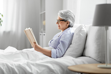 Image showing old woman in glasses reading book in bed at home