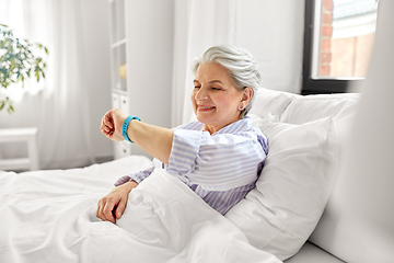 Image showing happy old woman with health tracker sitting in bed