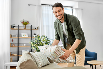 Image showing happy smiling man arranging sofa cushions at home