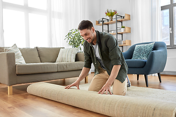 Image showing happy smiling young man unfolding carpet at home