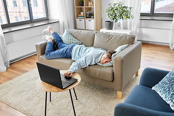 Image showing bored man with laptop lying on sofa at home