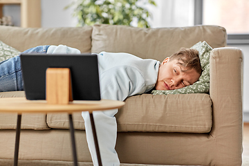 Image showing bored man with tablet pc lying on sofa at home