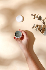 Image showing hand holding jar of blue cosmetic clay mask