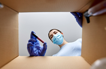 Image showing woman in mask unpacking parcel box with cosmetics