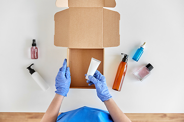 Image showing hands in gloves packing parcel box with cosmetics