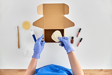 Image showing hands in gloves packing parcel box with cosmetics