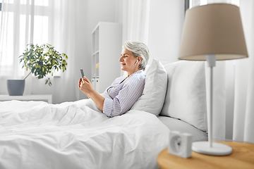 Image showing senior woman with smartphone and earphones in bed