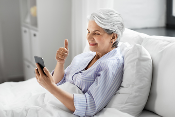 Image showing senior woman with phone having video call in bed