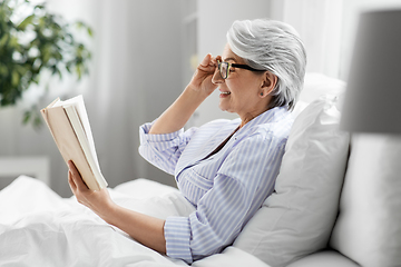 Image showing old woman in glasses reading book in bed at home