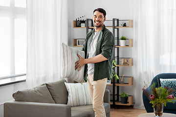 Image showing happy smiling man arranging sofa cushions at home