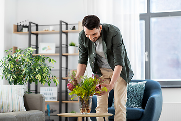 Image showing man placing flowers on coffee table at home