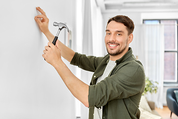 Image showing smiling man hammering nail to wall at home