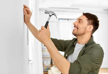 Image showing smiling man hammering nail to wall at home