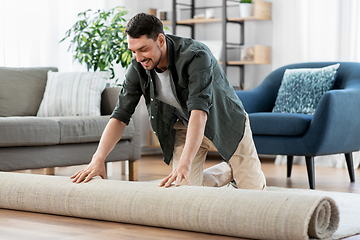 Image showing happy smiling young man unfolding carpet at home