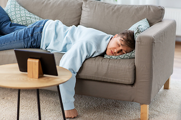 Image showing bored man with tablet pc lying on sofa at home