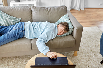 Image showing bored man with laptop lying on sofa at home