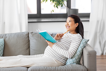 Image showing happy pregnant woman writing to diary at home