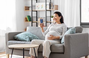 Image showing pregnant woman with phone and earphones at home