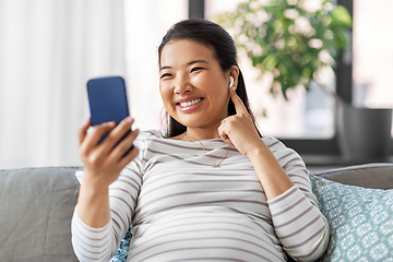 Image showing pregnant woman with phone and earphones at home