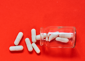 Image showing Pills spilling out of pill bottle on red. Top view with copy space. 