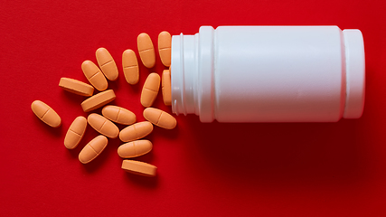 Image showing Pills spilling out of pill bottle on red. Top view with copy space. 