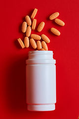 Image showing Pills spilling out of pill bottle on red. Top view with copy space. 