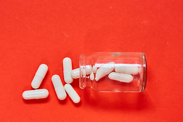 Image showing Pills spilling out of pill bottle on red. Top view with copy space. 